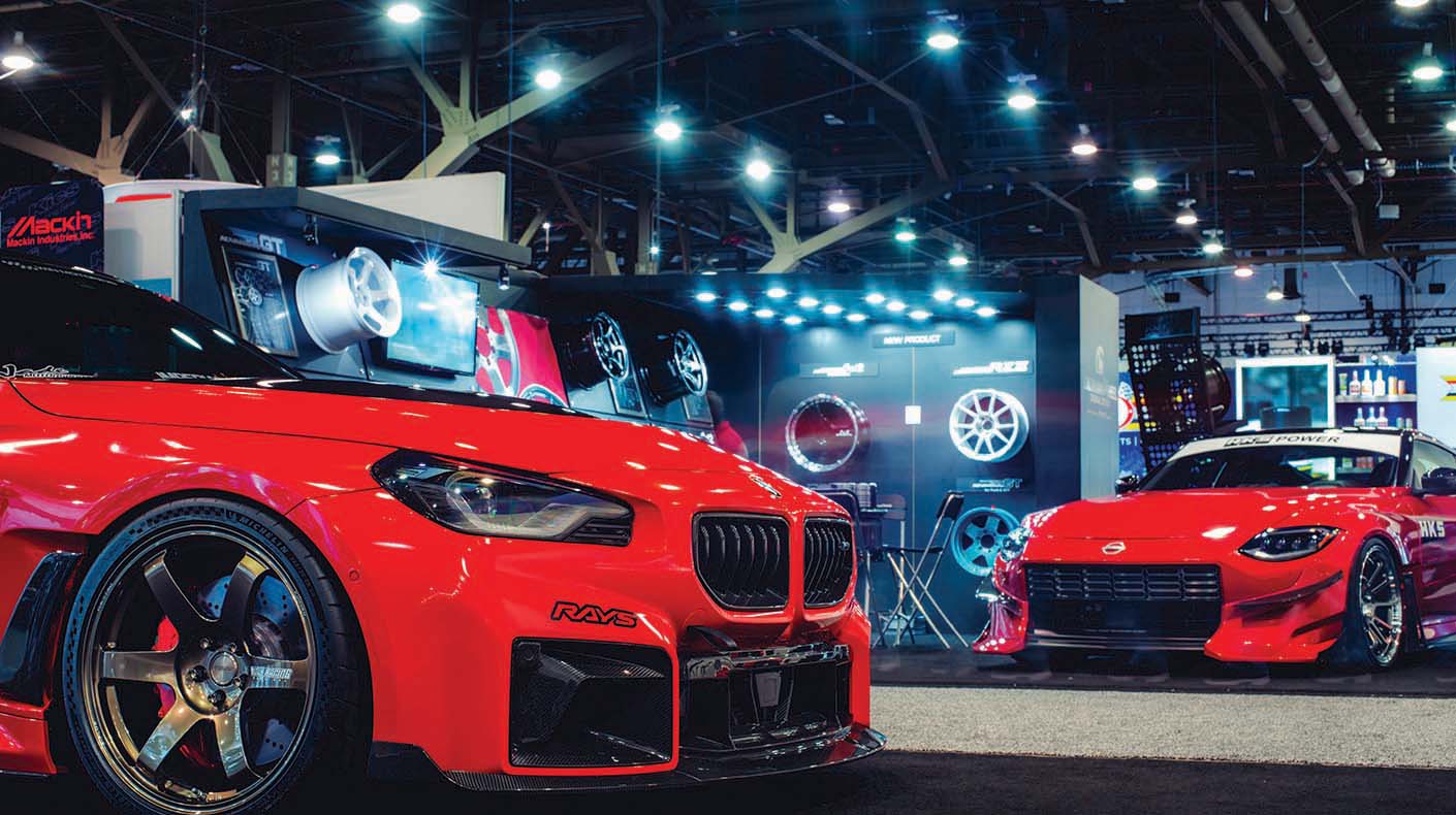 Red BMW and Nissan cars with wall of wheels on display in a booth.