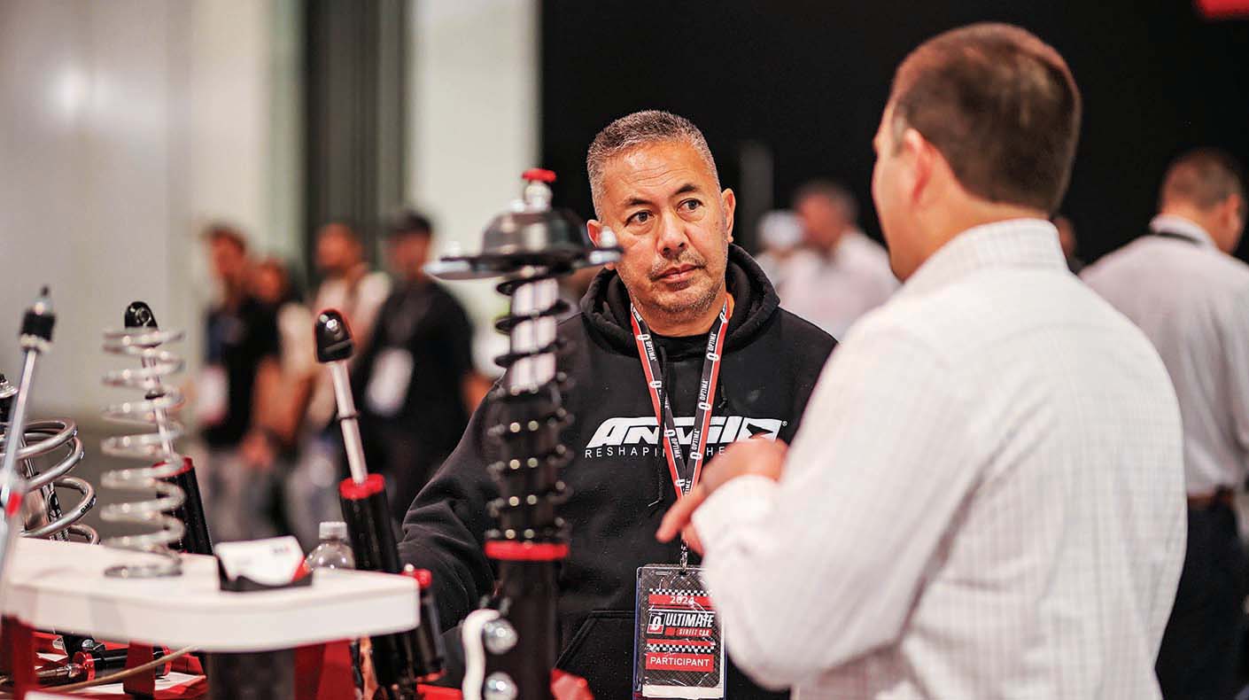 Two men standing and talking next to a display table with shocks and springs