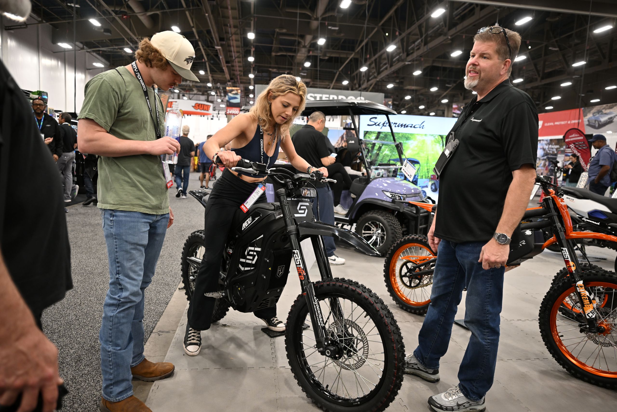 A model standing next to a black Meta electric dirt bike at the SEMA show, examining the handlebars