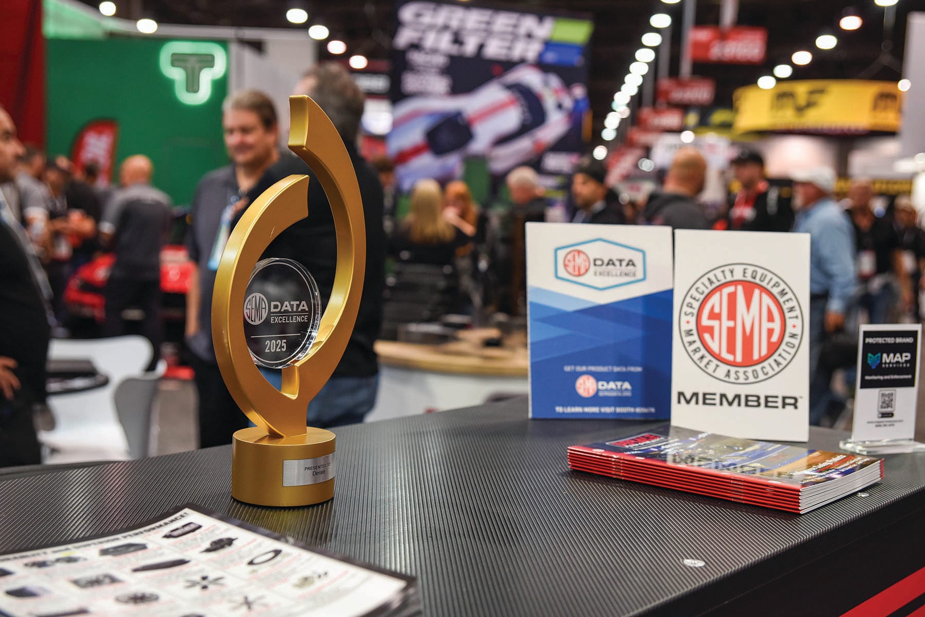 Gold SEMA Data Excellence 2025 trophy on a booth counter beside a SEMA Data sign, a SEMA Member sign and a stack of brochures